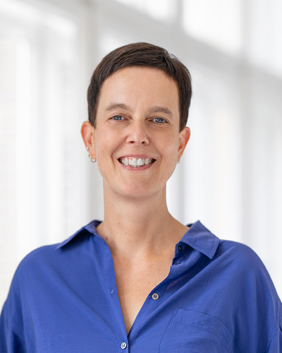 Frau in blauer Bluse vor hellem Hintergrund l&auml;chelt freundlich in die Kamera